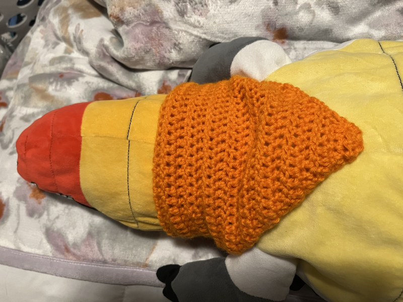 an underside view of a plush alligator wearing an orange bandana around its neck. the gator itself is white, grey, and black, with red, orange, and yellow stripes on its belly.